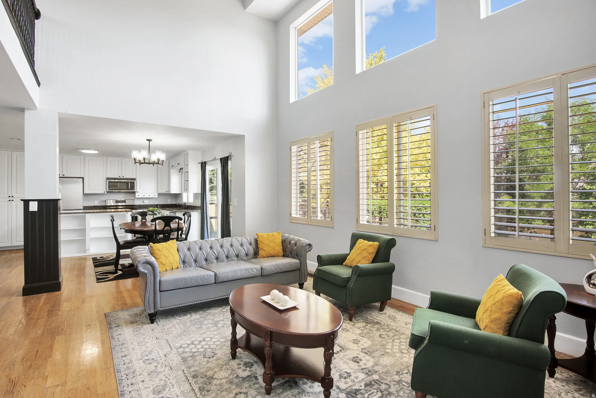 Vaulted ceiling, hardwood flooring, white kitchen cabinetry, dark countertops, and upper transom windows