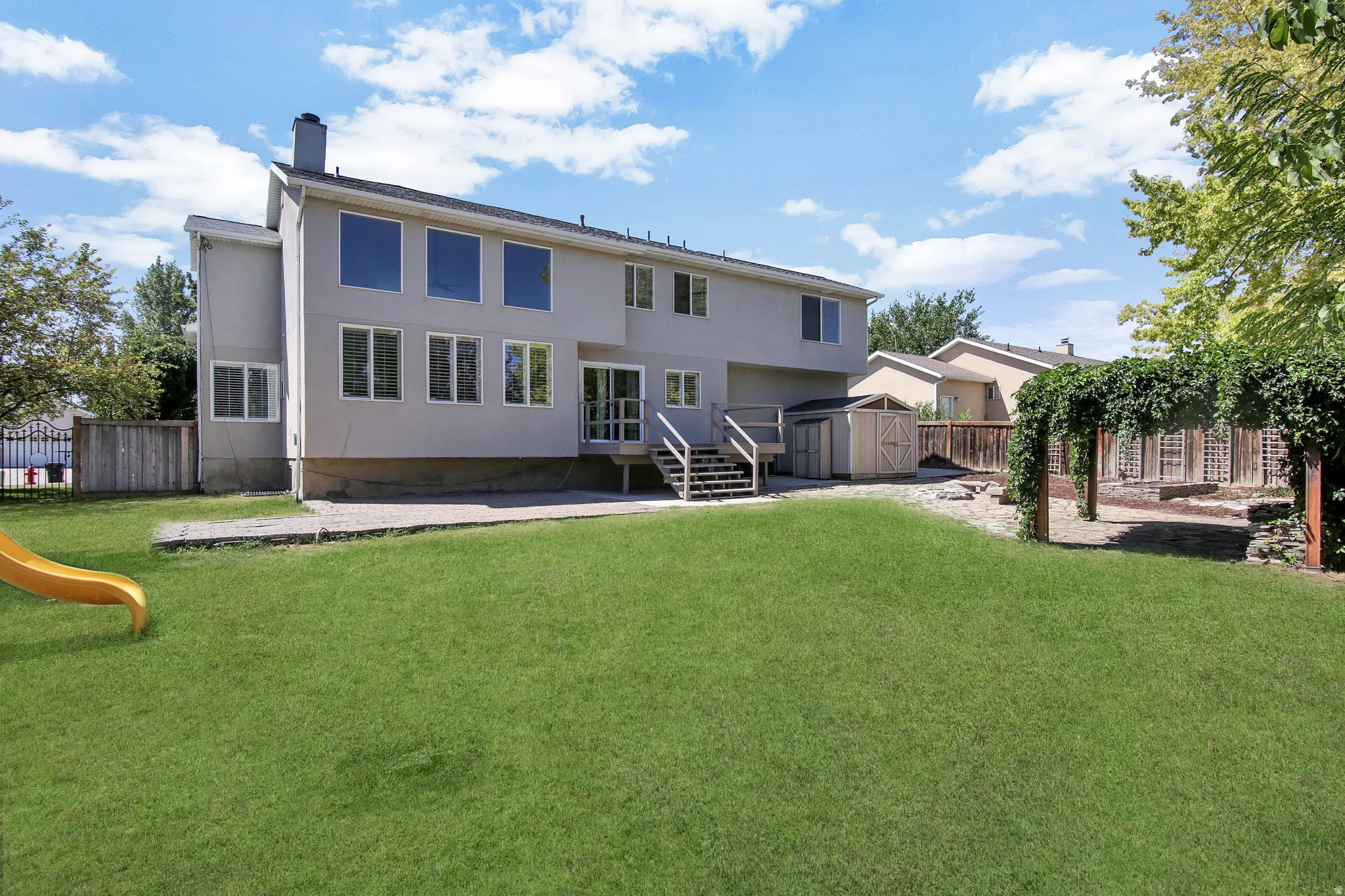 Expansive lawn area with a concrete patio, wood deck, and a detached shed