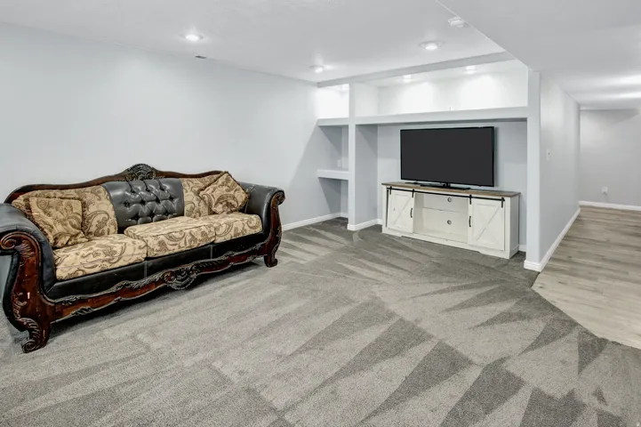 Recessed lighting throughout, gray patterned carpet, built-in shelving, white baseboards, and wood-finish flooring