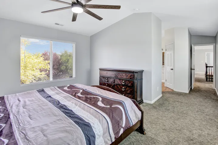 Vaulted ceiling, ceiling fan with integrated lighting, large window with blinds, light gray wall paint, and gray carpet flooring
