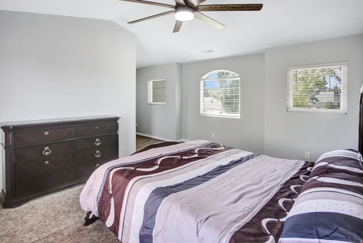 Vaulted ceiling with a ceiling fan, arched window, rectangular window with blinds, and neutral-toned wall paint
