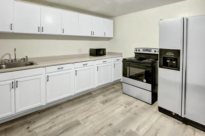 Updated kitchen featuring white shaker-style cabinetry, wood-finish flooring, a stainless steel sink, and light-toned countertops