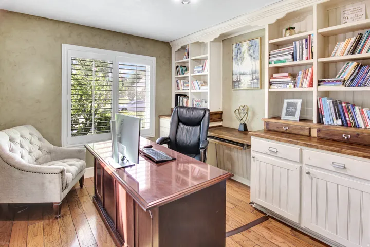 Hardwood flooring, custom built-in shelving, white plantation shutters, and a wood desktop surface