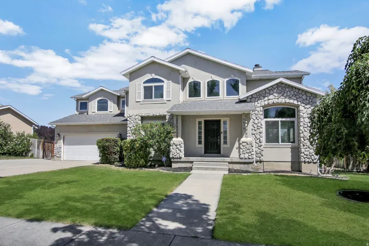 Stucco exterior with stone accents, arched windows, covered front entry, attached garage, and paved driveway