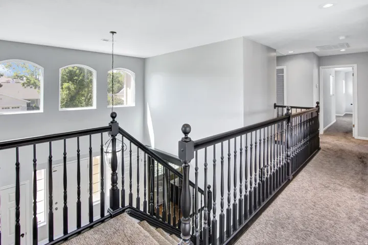 Upper landing featuring three arched windows, black painted balustrade, recessed lighting, and carpeted flooring