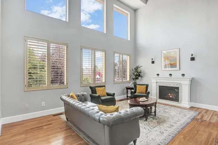 Vaulted ceilings with clerestory windows, plantation shutters, a fireplace with a stone surround, and wood-finish flooring