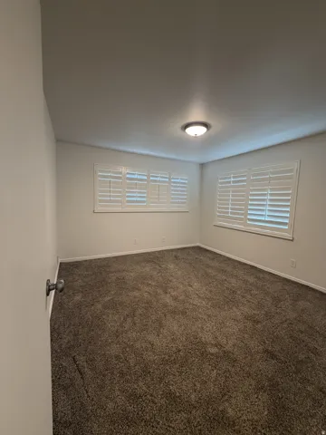 Plush carpeting and white wall paint complement multiple windows featuring white plantation shutters