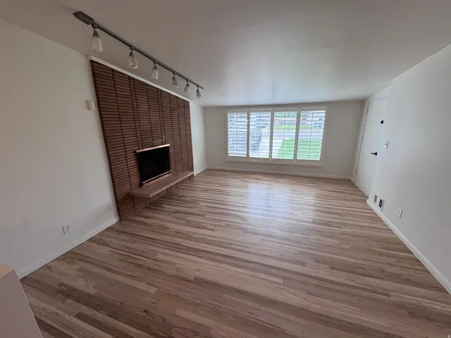 REfinished Red flooring, a gas fireplace featuring a brick surround, track lighting, and window shutters