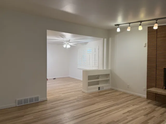 Wood-finish flooring throughout, integrated built-in shelving, white plantation shutters, and a slatted wood-panel fireplace surround