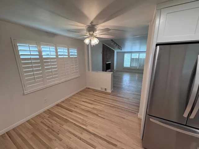 Hardwood flooring, white plantation shutters, stainless steel refrigerator, white cabinetry, and a ceiling fan with integrated lighting