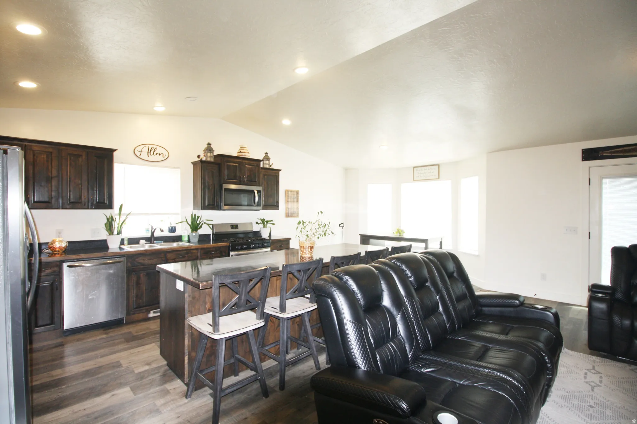 Vaulted ceiling, recessed lighting, dark wood cabinetry, stainless steel appliances, and wood-finish flooring