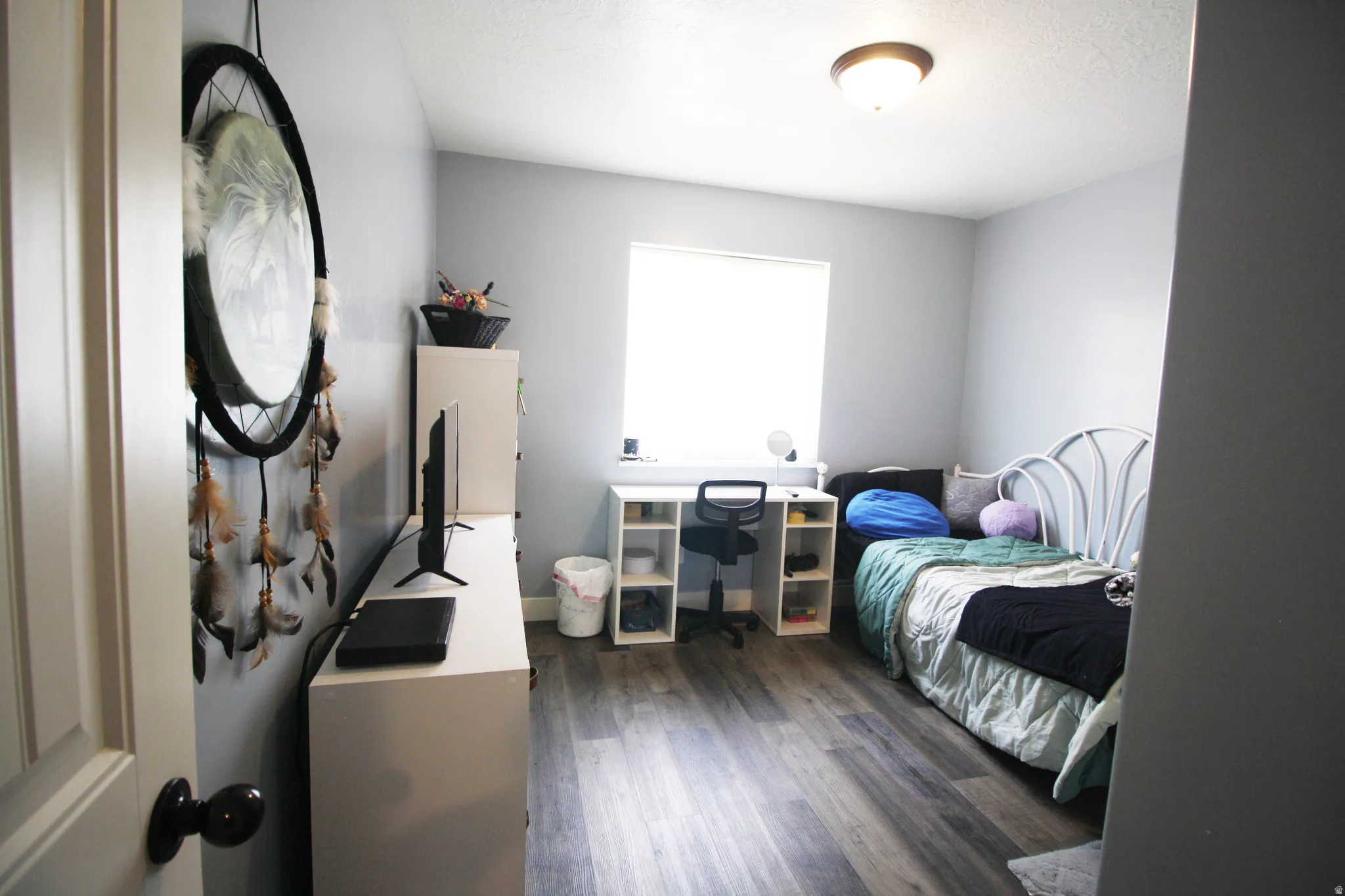 Wood-finish flooring with a ceiling-mounted light fixture, and a window with a roller shade