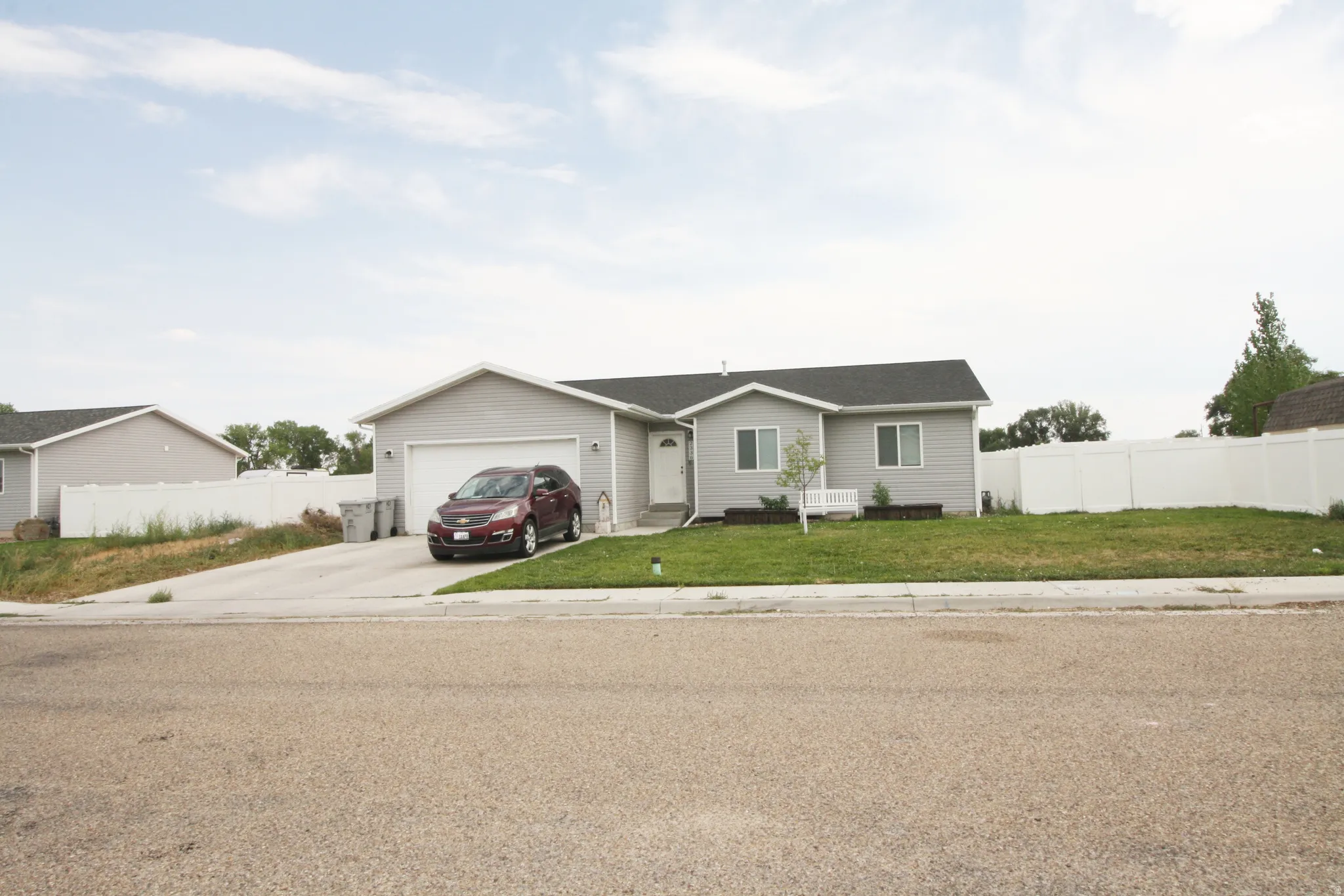 Single-story residence featuring light gray siding, an attached garage, a paved driveway, a green lawn, and a white privacy fence