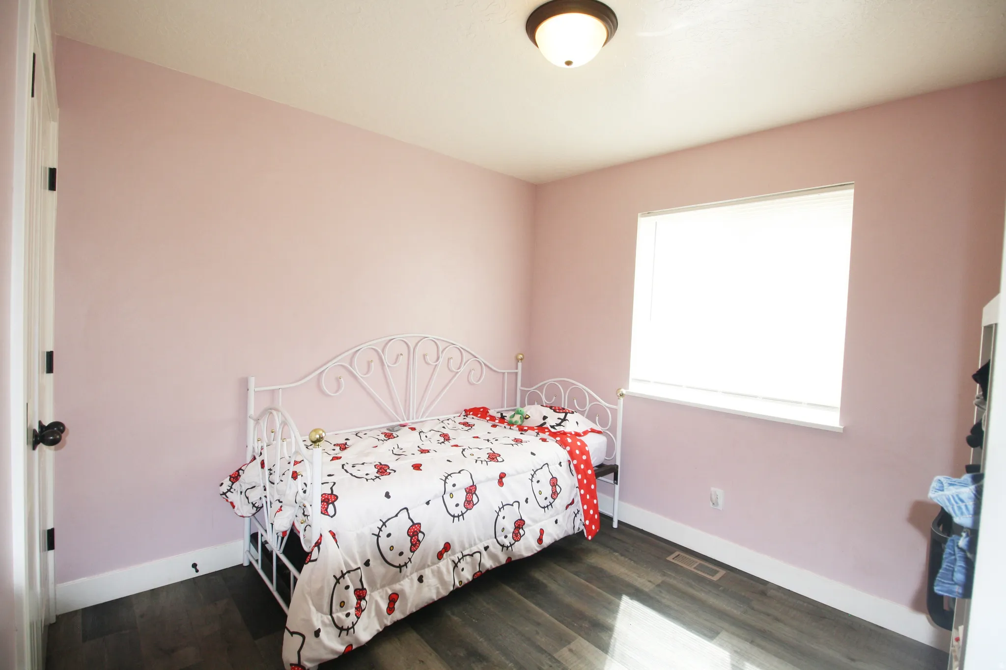 Wood-finish flooring, single window with roller shade, flush mount ceiling light fixture, white trim, and a white interior door with dark hardware