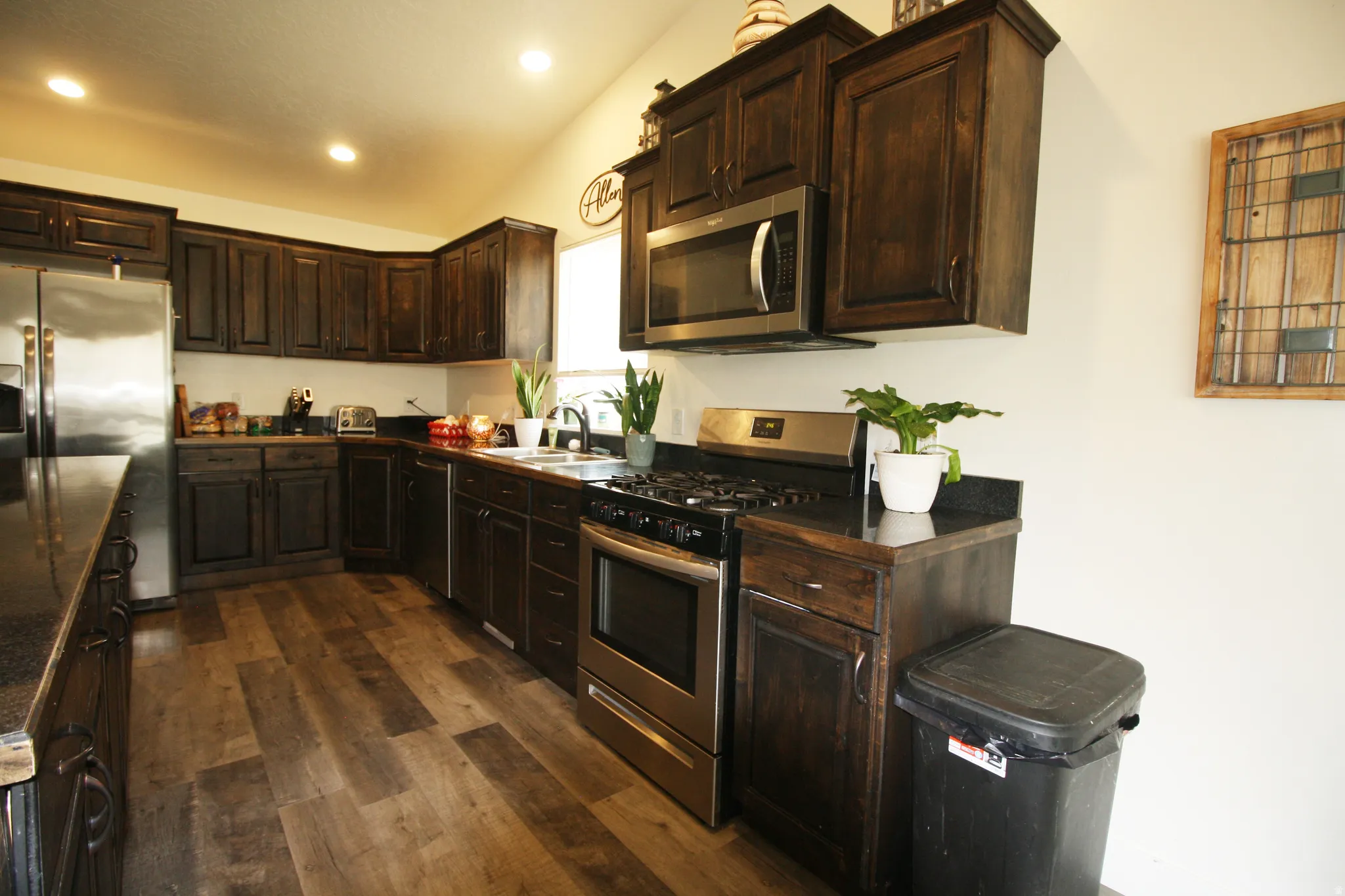 Kitchen featuring dark wood-finish cabinetry, stainless steel appliances, dark countertops, wood-finish flooring, and recessed lighting