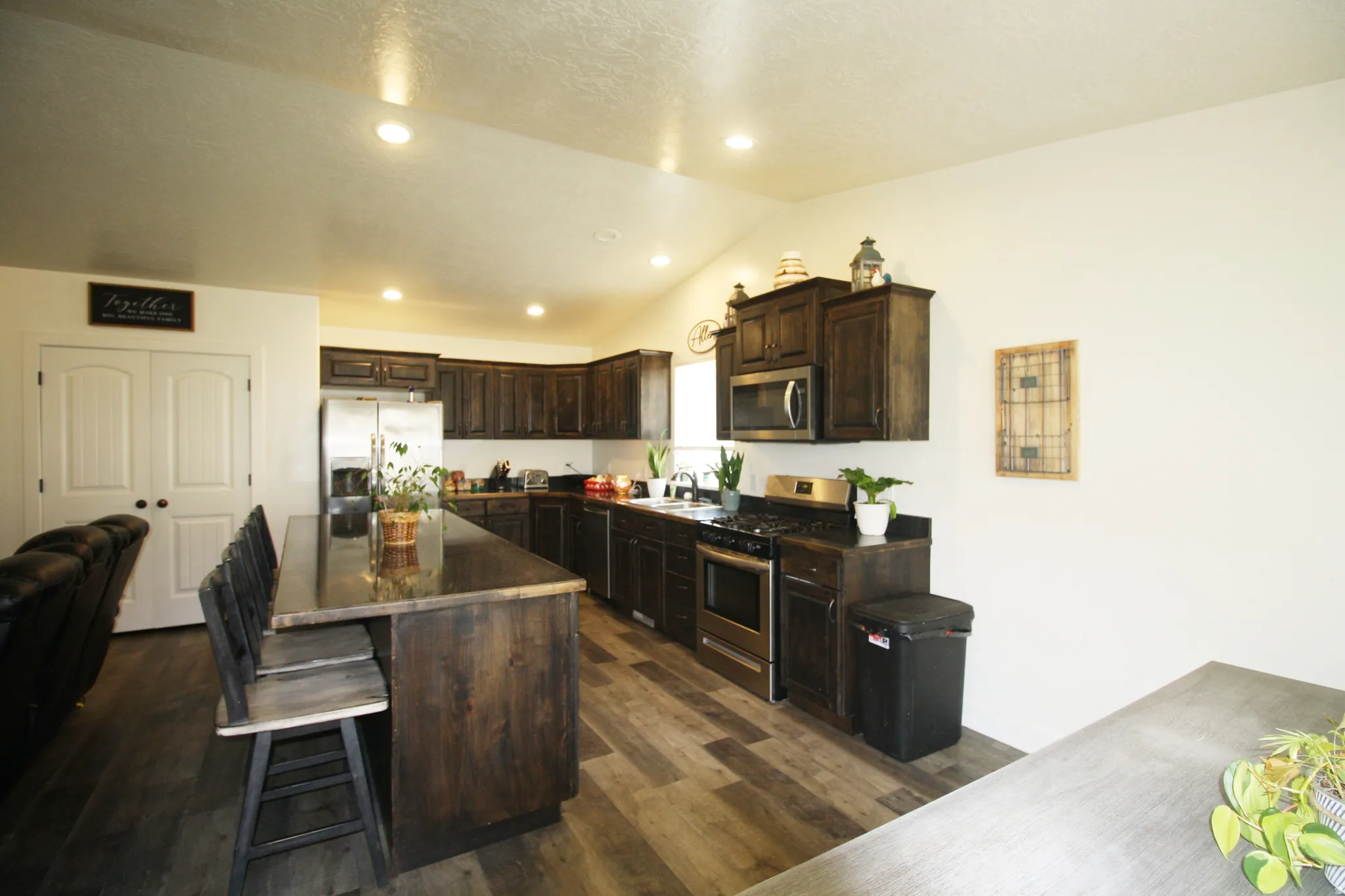 Kitchen featuring dark wood cabinetry, stainless steel appliances, wood-finish flooring, recessed lighting, and a large central island with seating