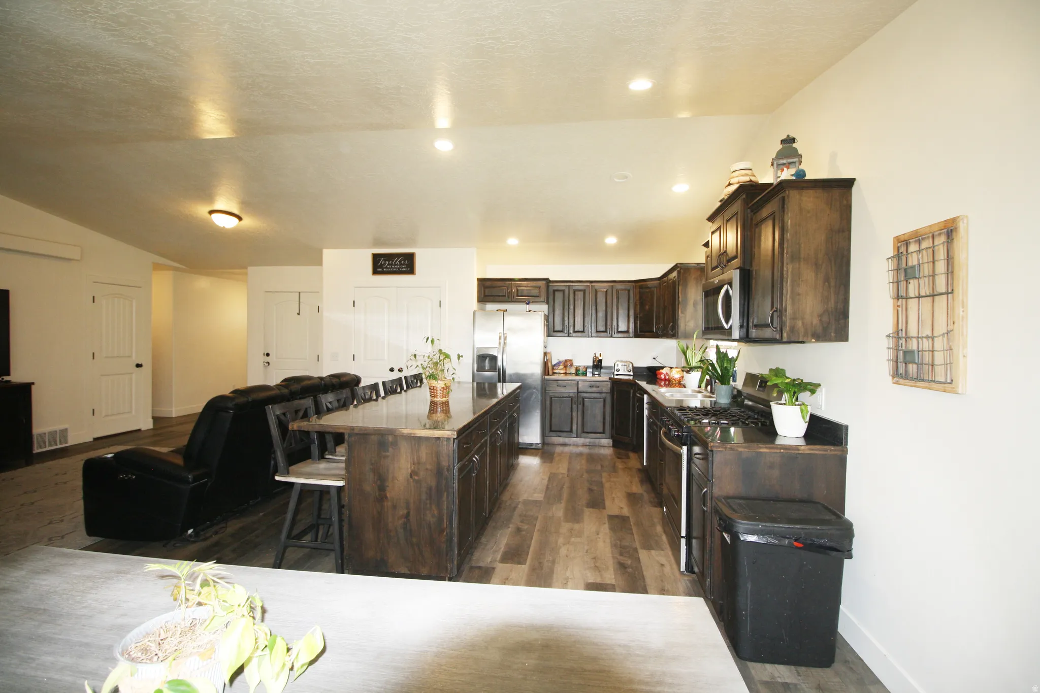 Open-concept kitchen featuring dark wood cabinetry, a large kitchen island with counter seating, stainless steel appliances, and wood-finish flooring