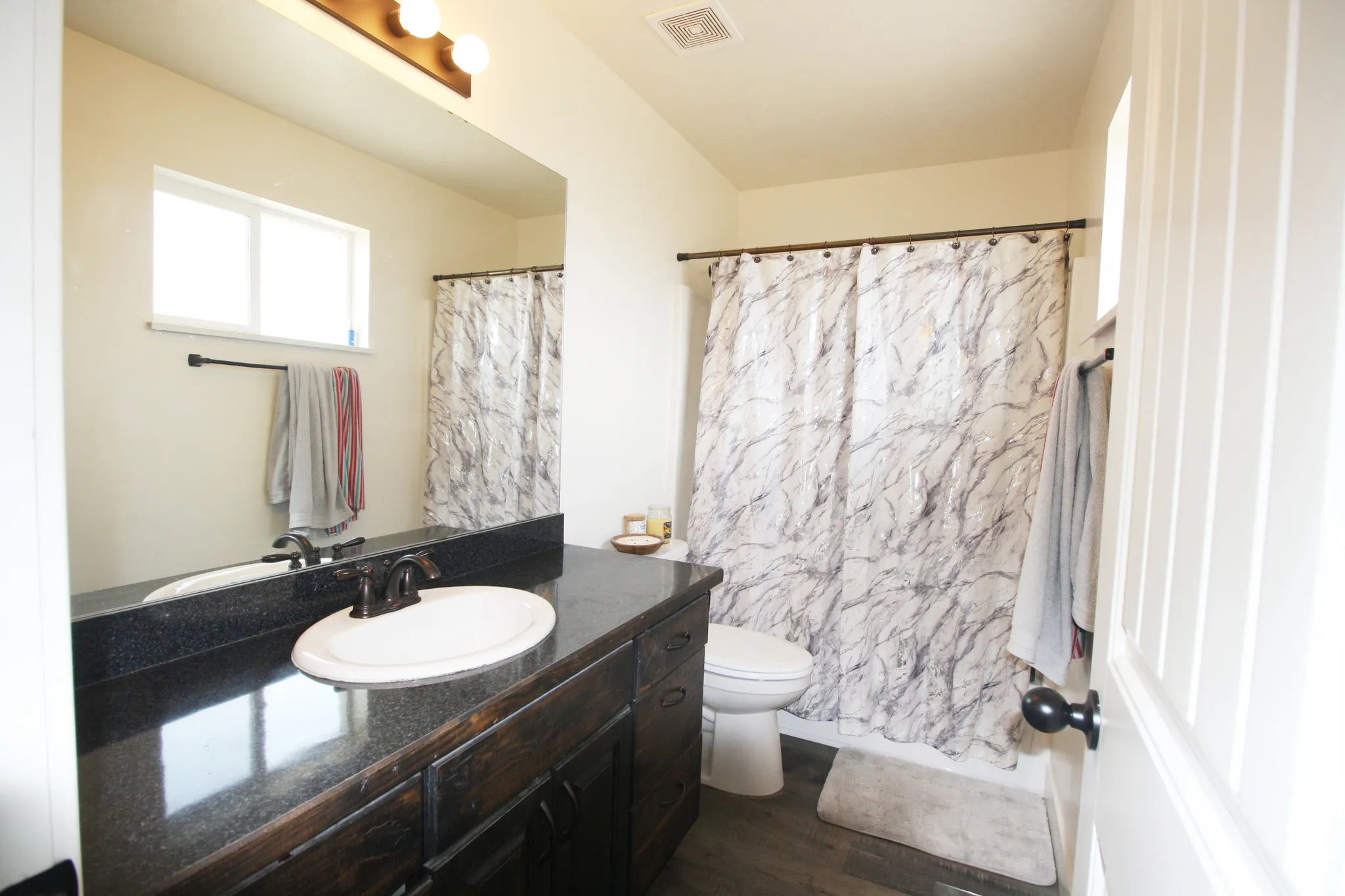 Bathroom featuring a dark wood-finish vanity, solid surface countertop, undermount sink, and wood-finish flooring