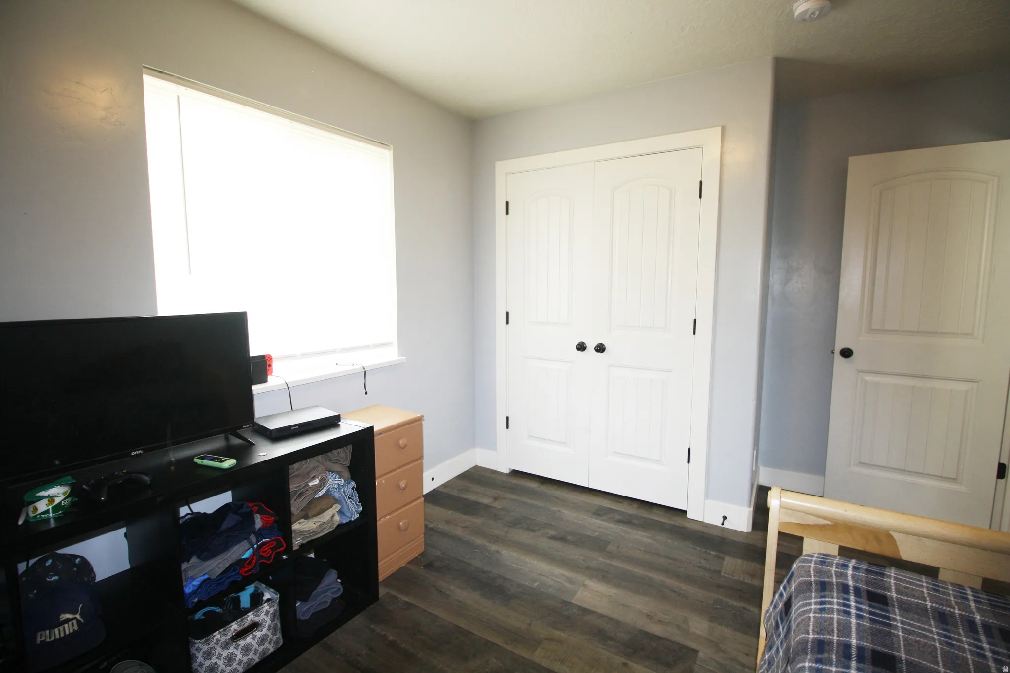 Wood-finish flooring, white paneled doors, and a window with roller blinds