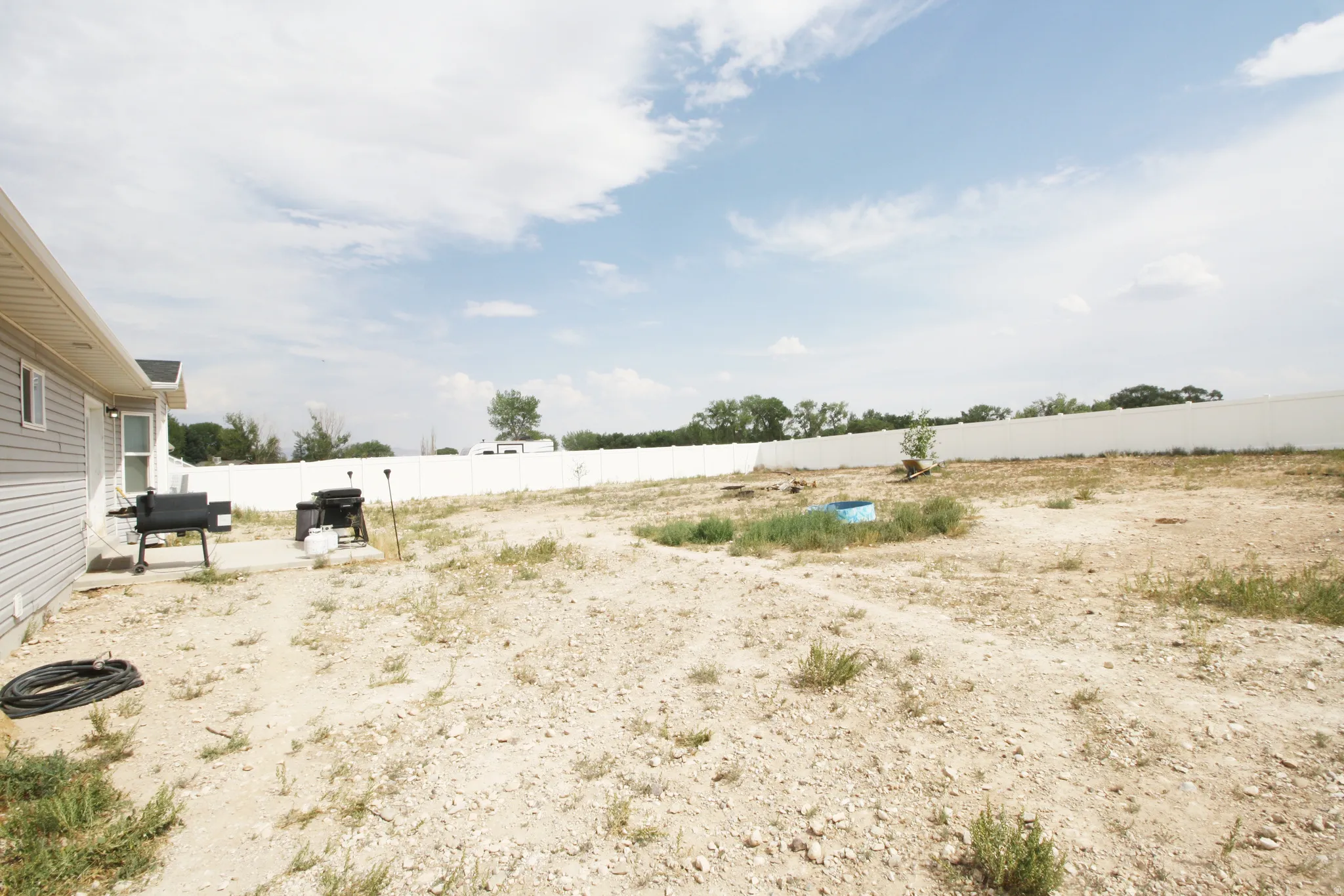 Expansive undeveloped yard, vinyl siding exterior, white privacy fencing, and a concrete patio