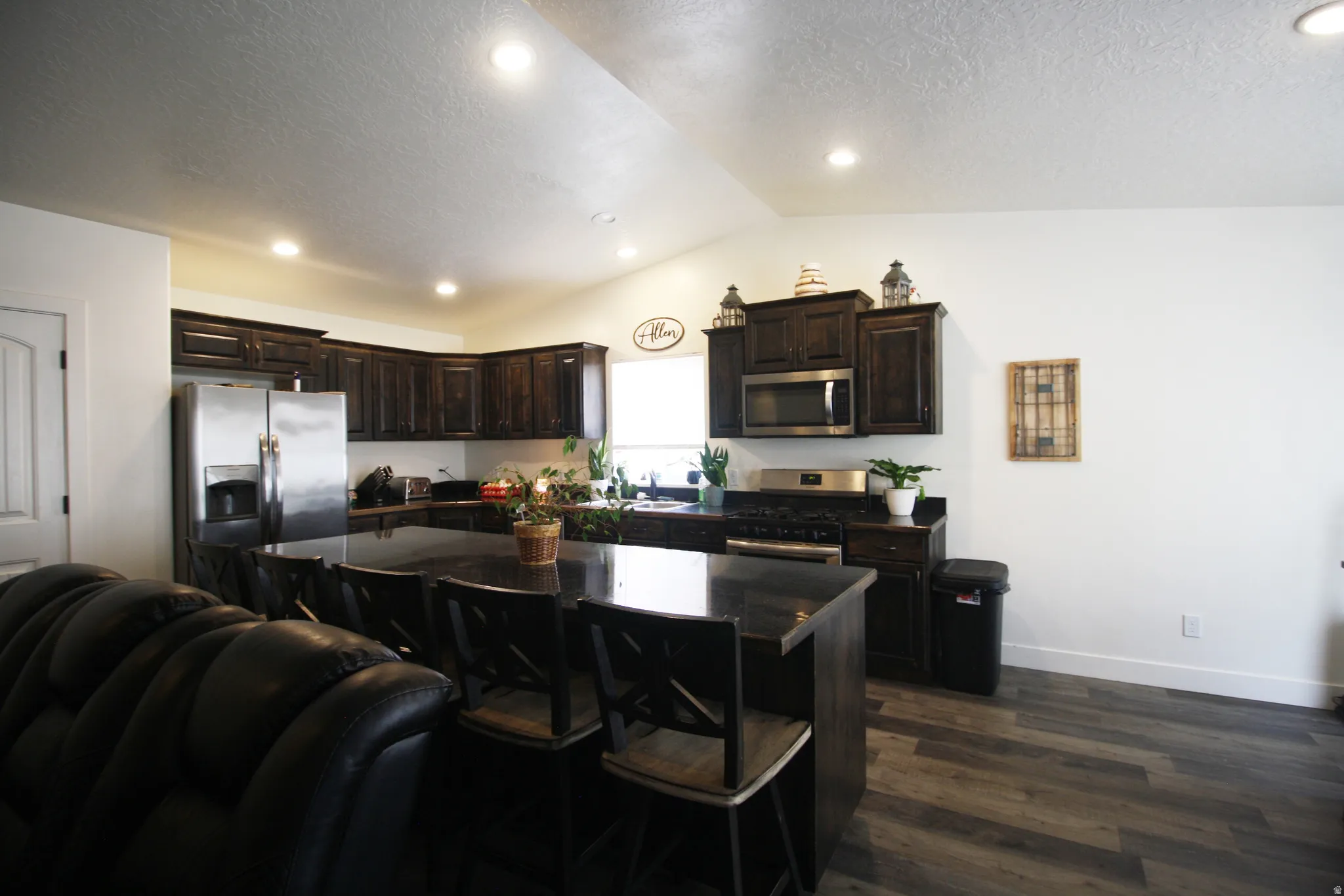 Kitchen featuring dark wood-finish cabinetry, stainless steel appliances, a large island with seating, and wood-finish flooring