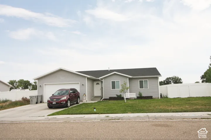 Ranch-style exterior with gray siding, attached garage, and a white picket fence