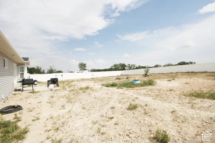 Expansive undeveloped yard, vinyl siding exterior, white privacy fencing, and a concrete patio
