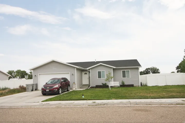 Ranch-style exterior with gray siding, attached garage, and a white picket fence