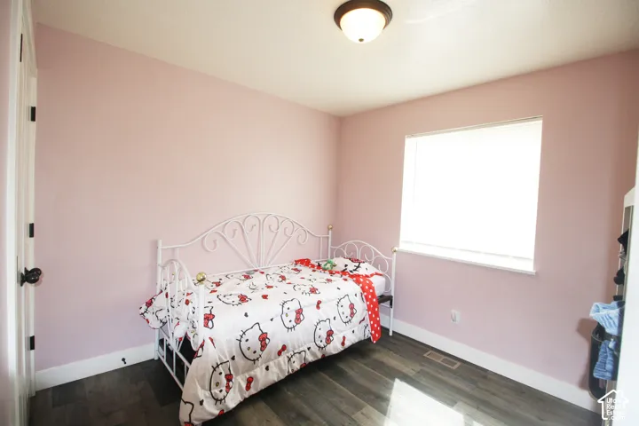Wood-finish flooring, single window with roller shade, flush mount ceiling light fixture, white trim, and a white interior door with dark hardware