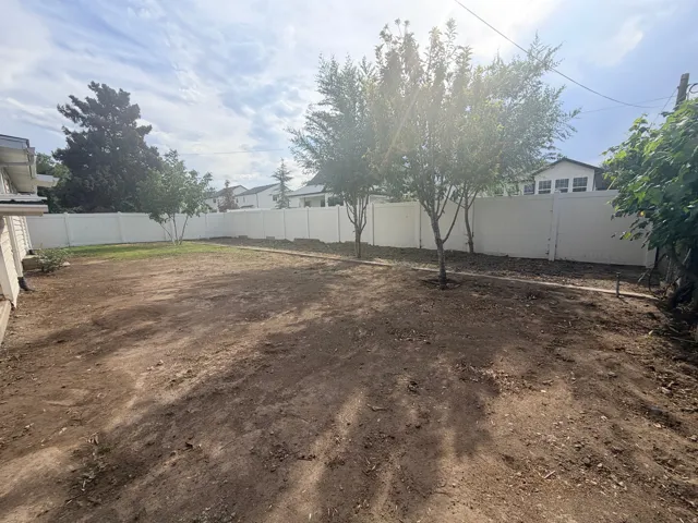Expansive yard space featuring a white privacy fence and established trees