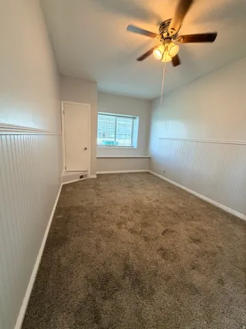 Neutral wall paint, beadboard wainscoting, window with blinds, ceiling fan with integrated lighting, and carpeted flooring