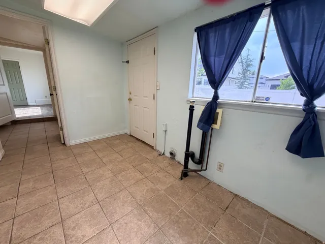 Bright, light-filled room featuring tile flooring, large windows with blue drapery, skylight above, and white painted walls