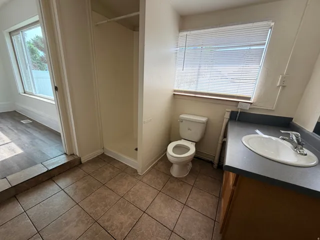 Bathroom featuring a walk-in shower, window with blinds, tile flooring, and a single vanity with an integrated sink