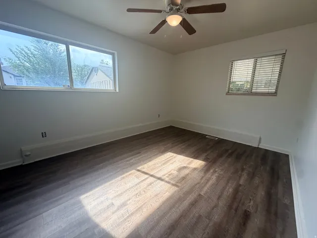 Wood-finish flooring, white walls, two windows, and a ceiling fan with integrated lighting