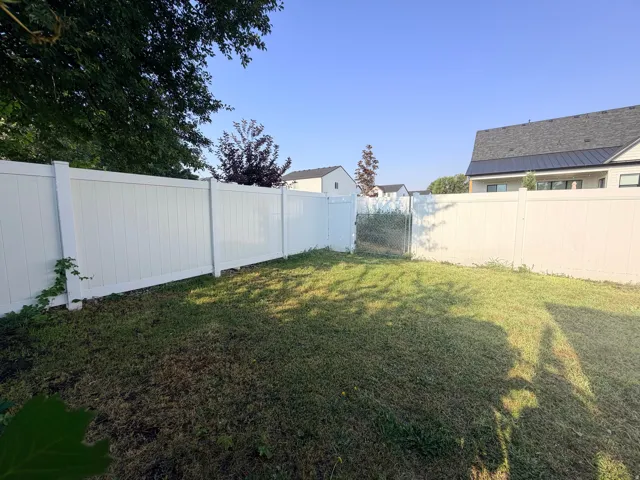 Expansive backyard featuring a white privacy fence and a chain-link gate