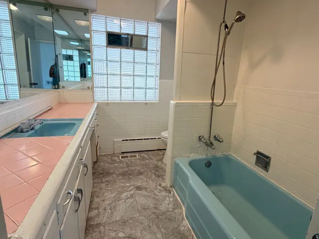 Bathroom featuring a full vanity with dual integrated sinks, an integrated bathtub, and a glass block window