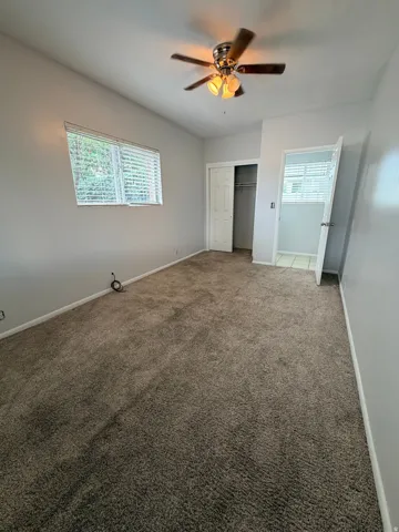 Carpeted flooring, window with blinds, ceiling fan with integrated lighting, closet with bi-fold doors, and an open doorway