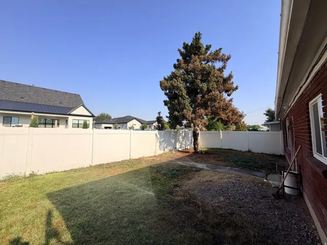 Expansive backyard area featuring a white privacy fence, mature trees, and a brick exterior