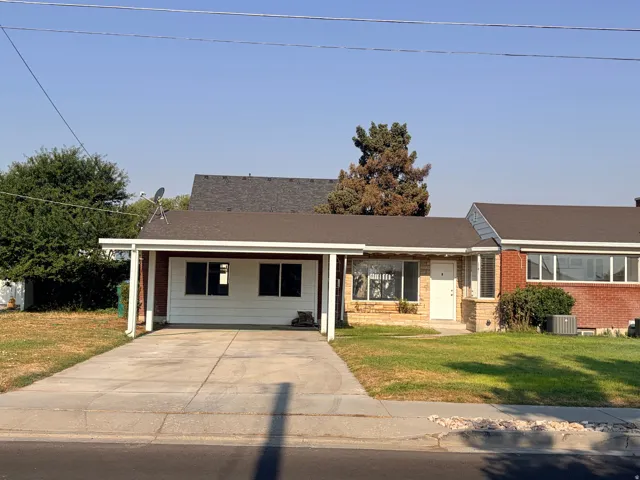 Brick and stone exterior with a covered carport, concrete driveway, and front lawn