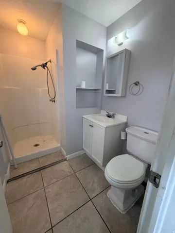 Tiled flooring, white shower stall with mounted shower head, built-in shelving, vanity with white cabinet, and a wall-mounted medicine cabinet