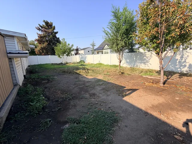 Expansive backyard featuring a white vinyl fence, mature trees, and a building exterior with horizontal siding