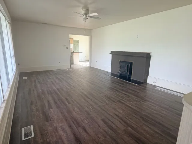 Wood-finish flooring, white walls, ceiling fan, and a fireplace with a black mantel