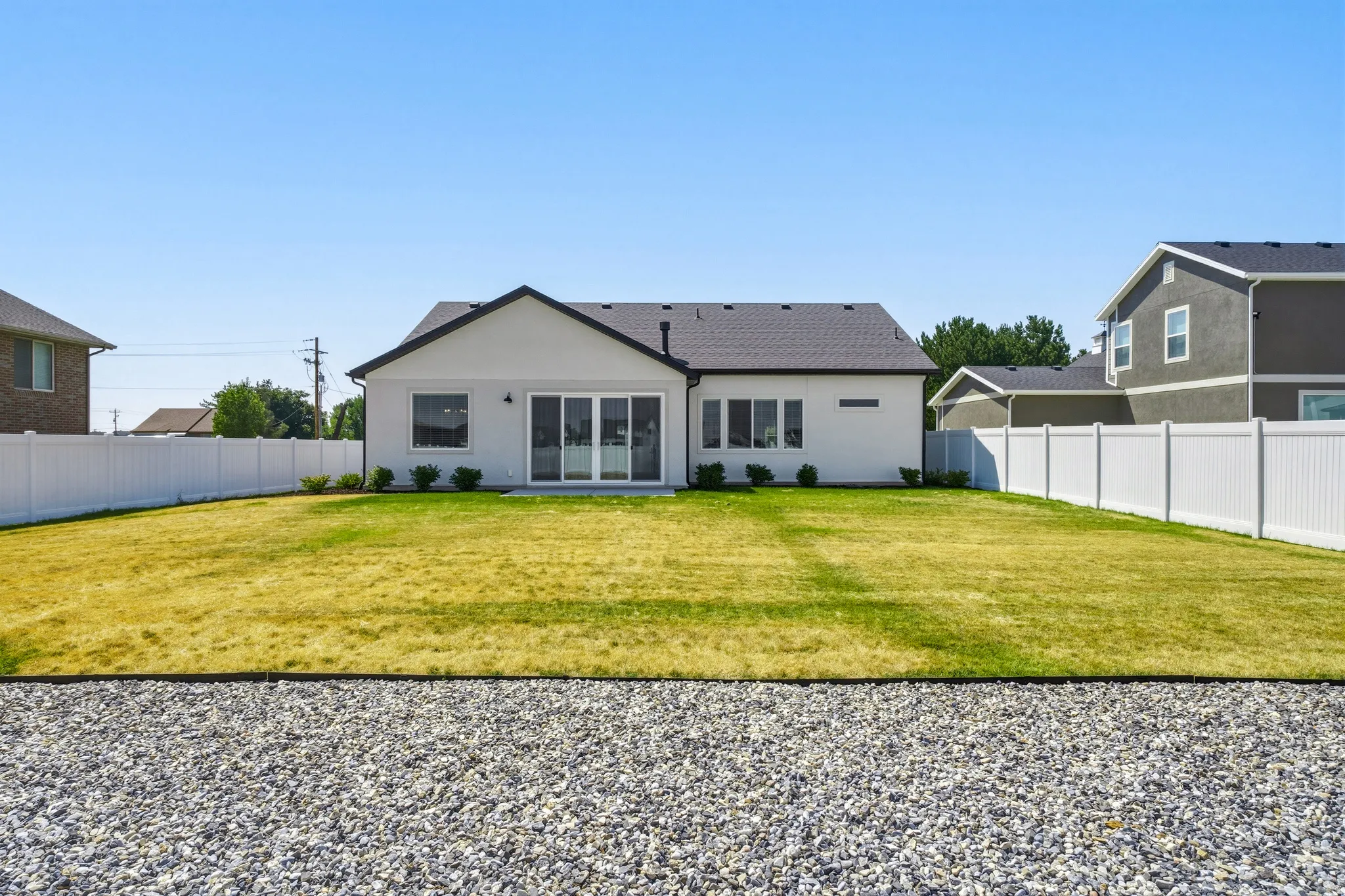Expansive backyard featuring a manicured lawn with mature landscaping, bordered by white vinyl fencing