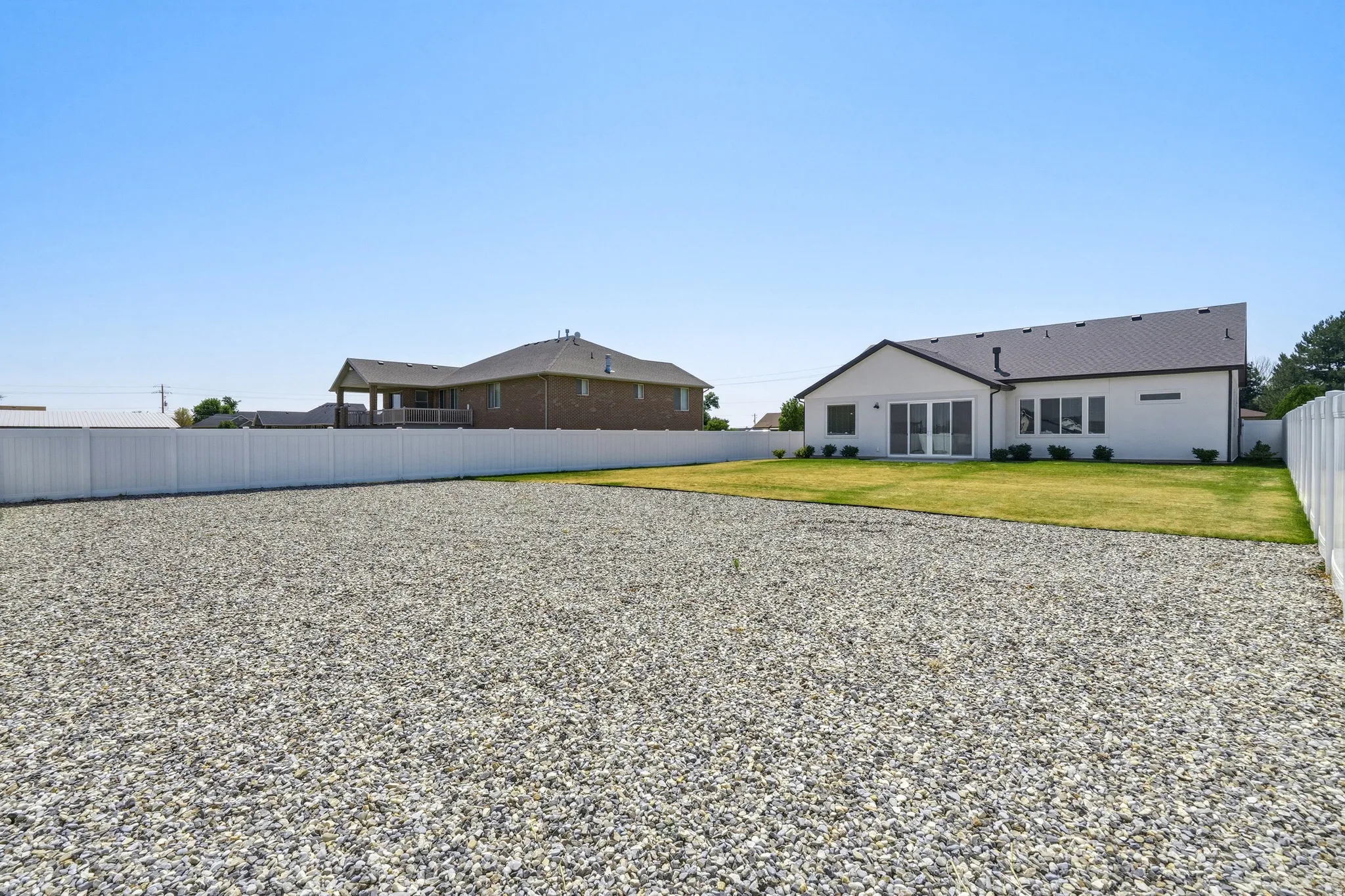 Spacious residential property featuring a modern white ranch-style home with gabled roofline, situated on an expansive gravel lot with manicured lawn sections