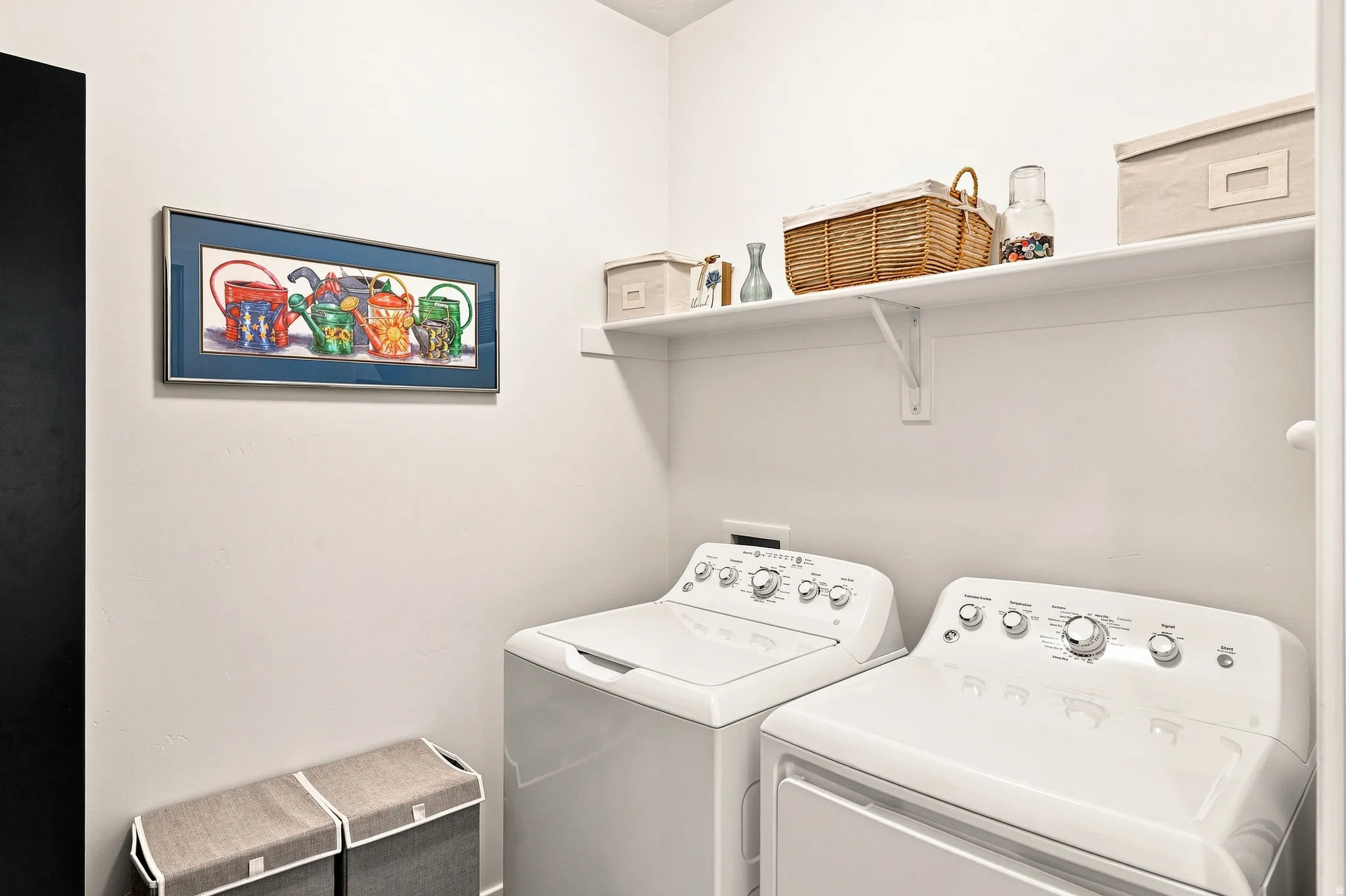 Dedicated laundry room featuring side-by-side washer and dryer with full-size capacity, open shelving with woven storage baskets, and bright white finishes throughout