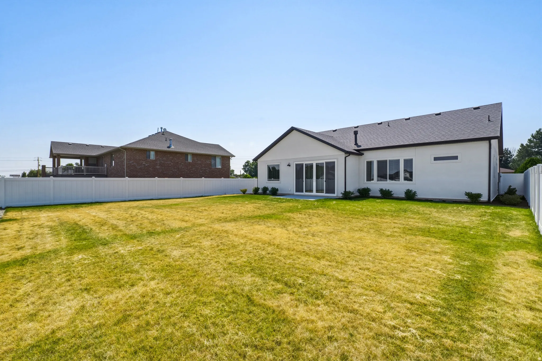Spacious backyard featuring a white vinyl privacy fence, a newly constructed white exterior, a dark asphalt shingle roof, and a multi-panel sliding glass door