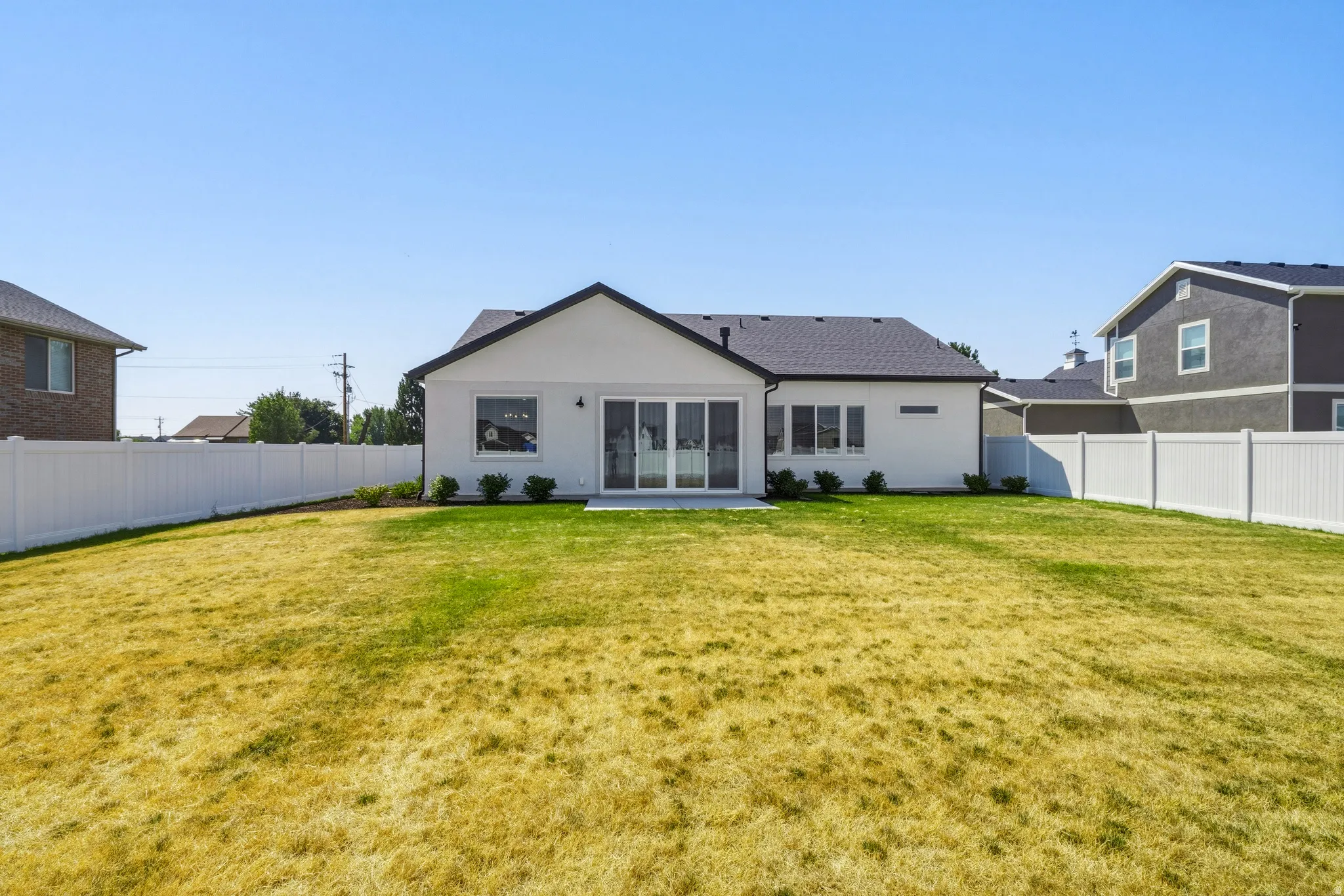 Expansive rear yard featuring a manicured lawn bordered by white vinyl fencing, with direct access from the home's sliding glass doors