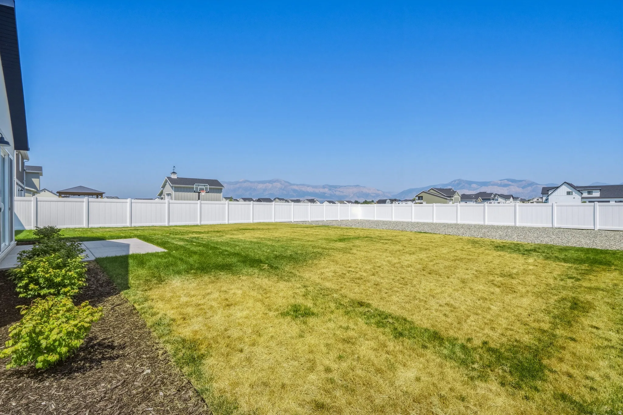 Expansive backyard featuring a manicured lawn, a concrete patio, and a white privacy fence