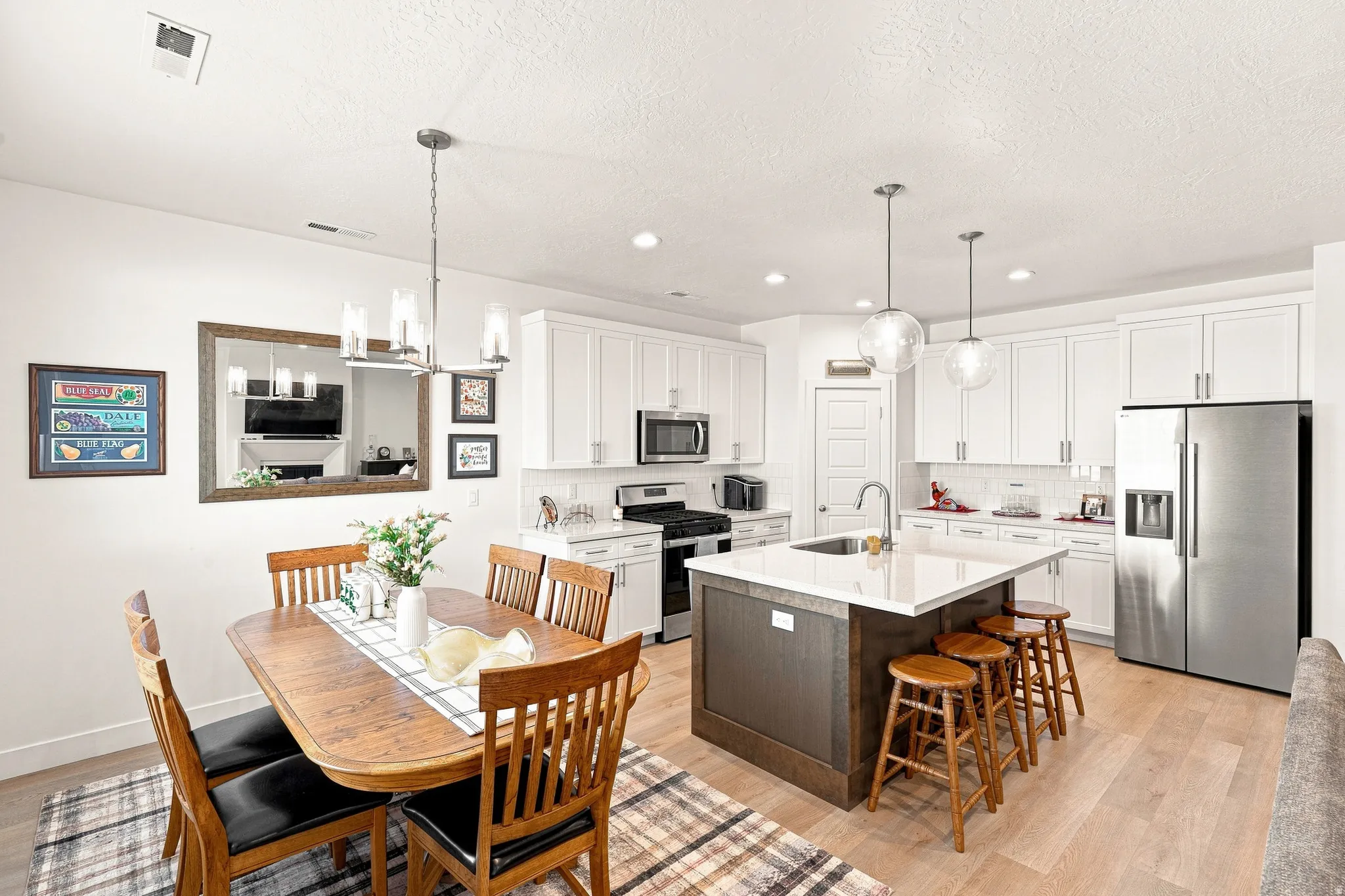 Open-concept layout featuring a kitchen island with seating, stainless steel appliances, white cabinetry, recessed lighting, and wood-finish flooring