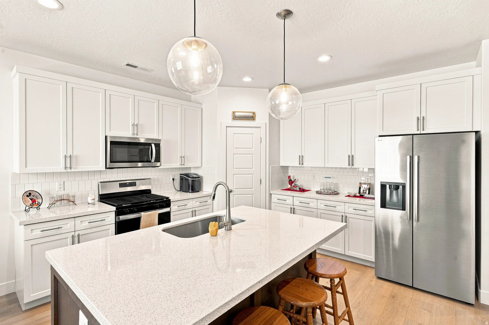 White shaker cabinetry, stainless steel appliances, quartz countertops, subway tile backsplash, and two pendant light fixtures